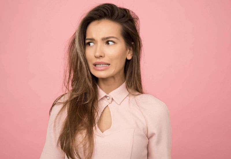 Woman with a worried expression against a pink background