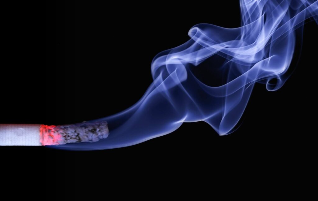 Lit cigarette with smoke curling against a black background
