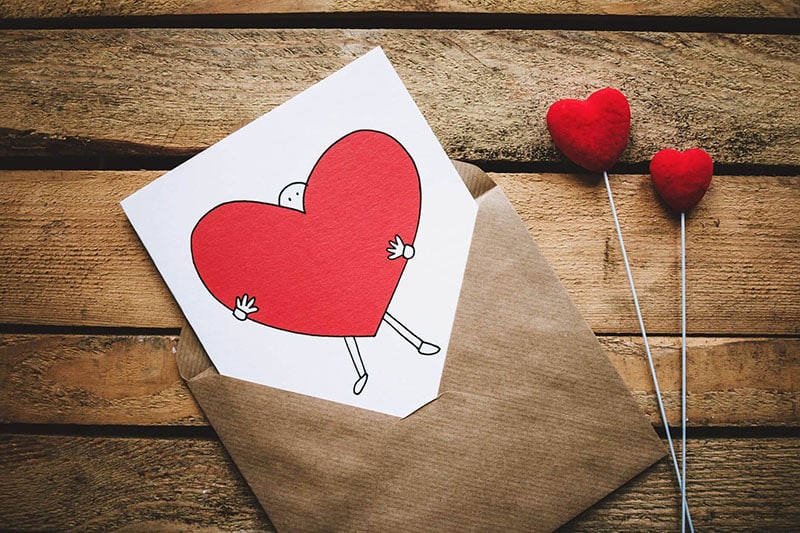 Heart-shaped Valentine's card in a kraft envelope with two red hearts on wood