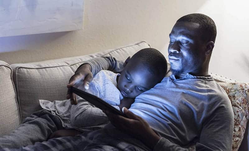Father and young son relaxing on a couch looking at a tablet