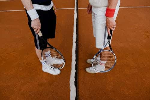 Two tennis players standing at the net, legs and rackets visible