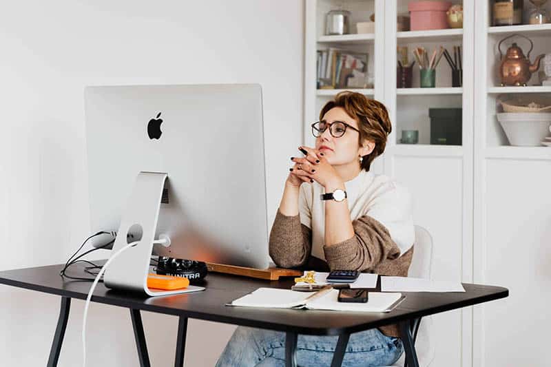 Woman with glasses sitting thoughtfully at a desk with a computer