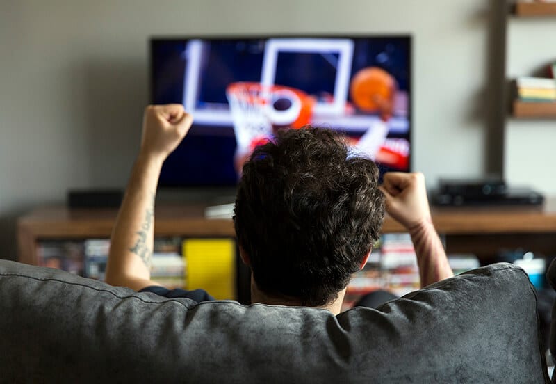 Man cheering in front of a TV showing basketball