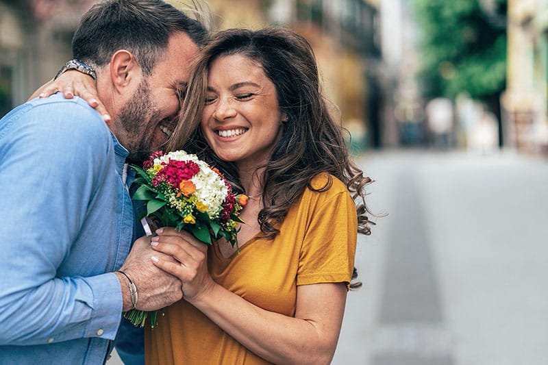 Smiling couple embracing, woman holding a bouquet of flowers