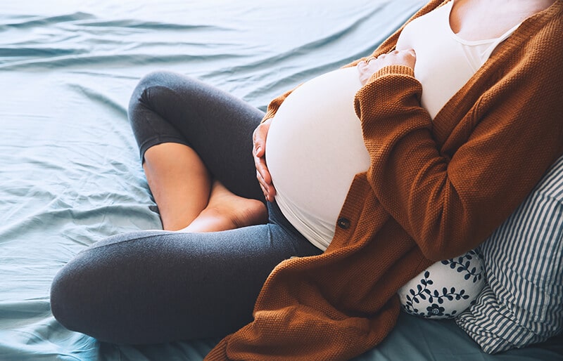Pregnant woman sitting on a bed holding her belly