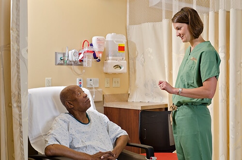 Nurse in green scrubs talking with a patient in a hospital room