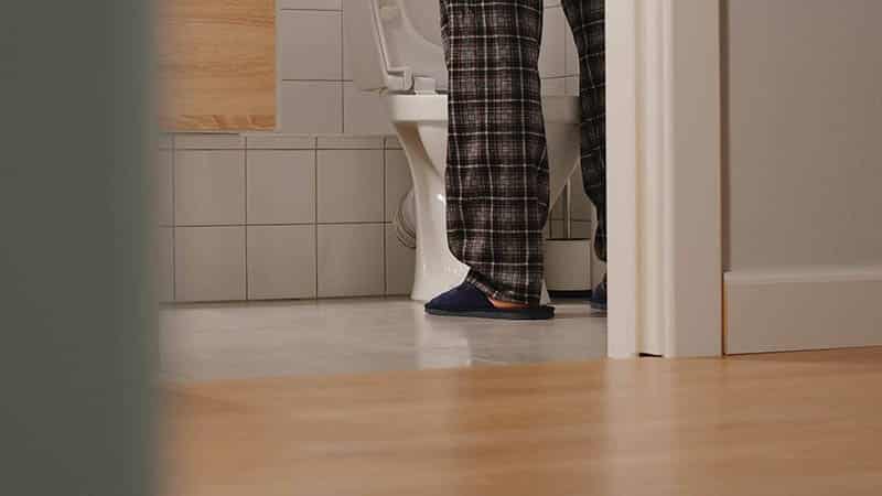 Man in pajama pants standing at a toilet in a bathroom