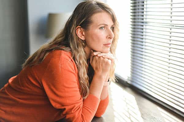 Thoughtful woman in an orange top looking out a window