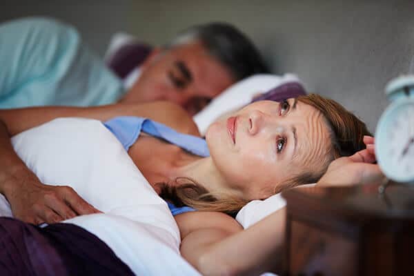 Woman lying awake in bed next to a sleeping man