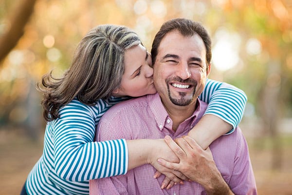 Smiling man being hugged and kissed on the cheek by his wife