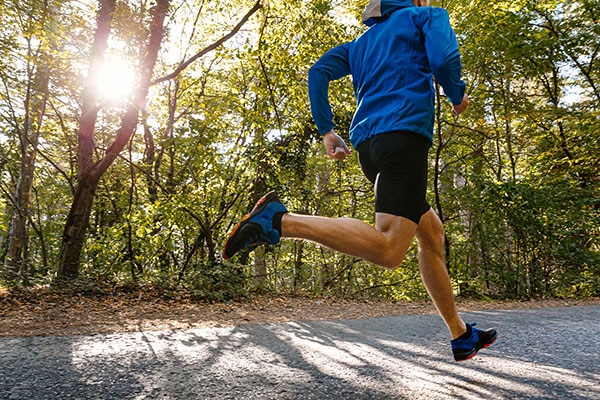 Male runner jogging on a tree-lined road in sunlight