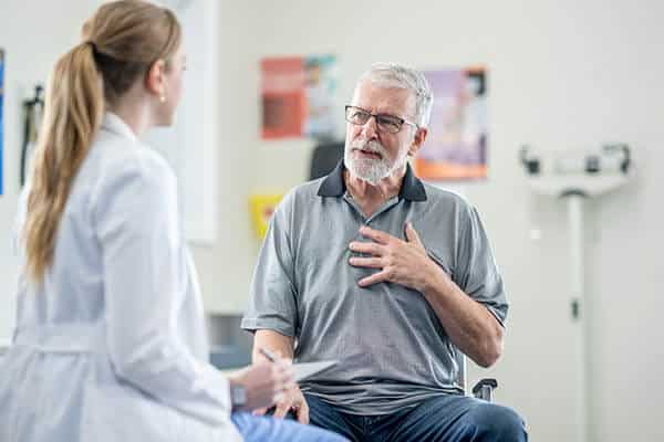 Female doctor talking with an older male patient who has a hand on his chest