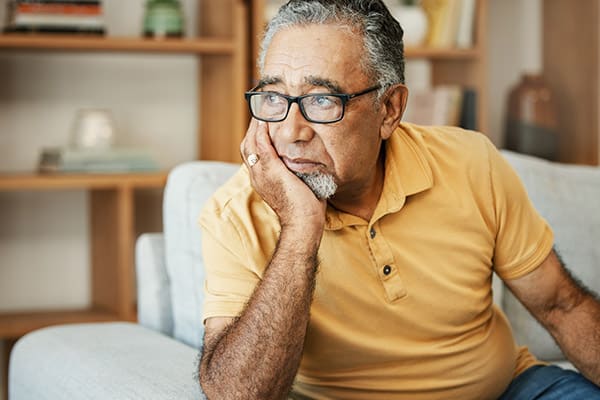 Thoughtful older man resting his chin on his hand on a sofa