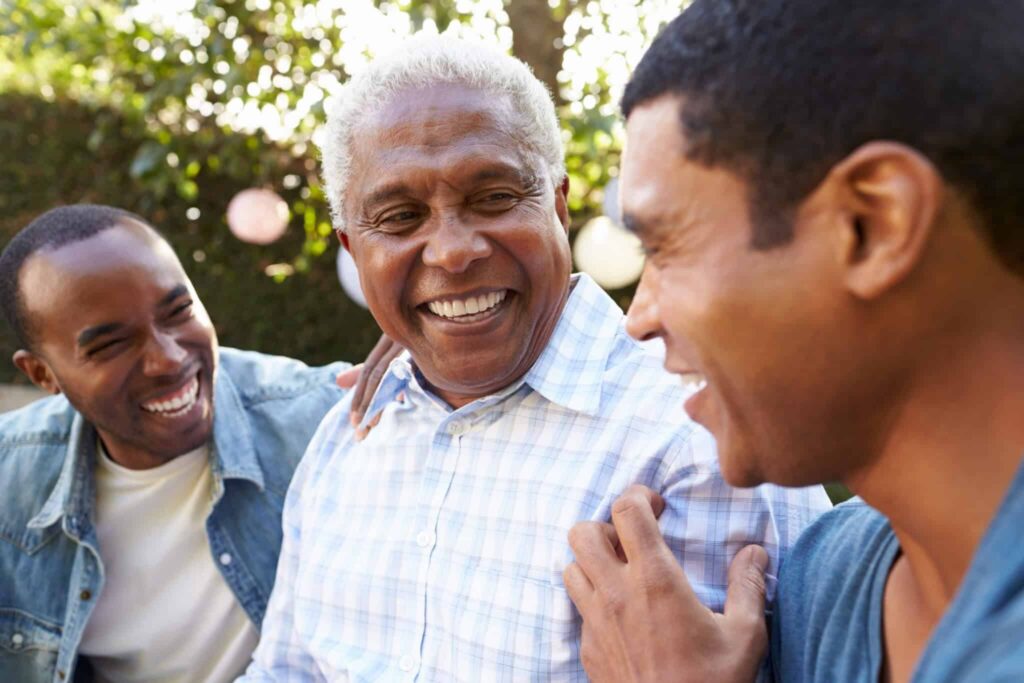Three smiling Black men of different generations laughing together outdoors
