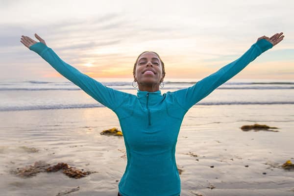 Woman with arms outstretched smiling on a beach at sunrise