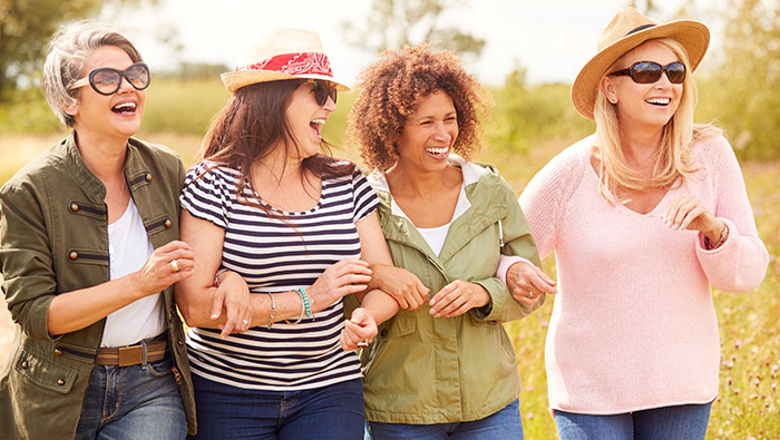 Four mature women friends walking arm in arm outdoors, laughing