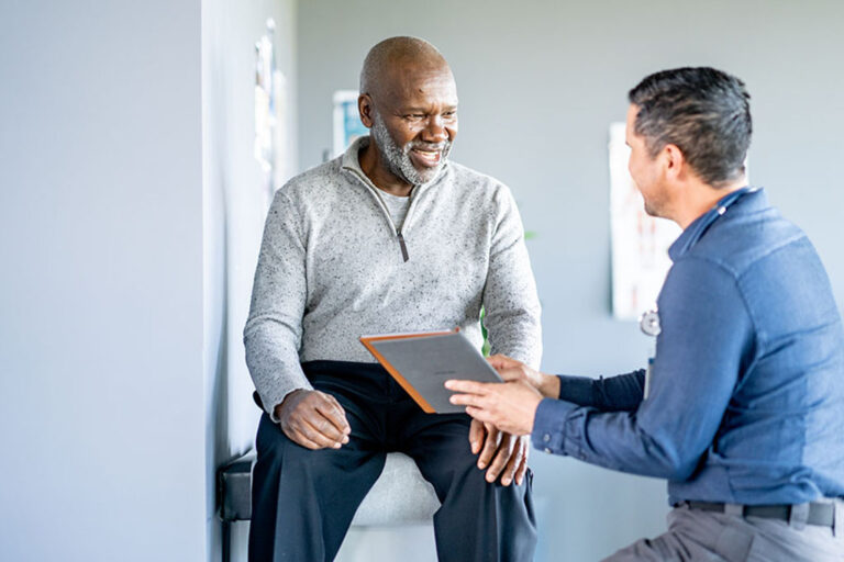 Smiling senior man sitting on an exam table while a provider shows him a tablet