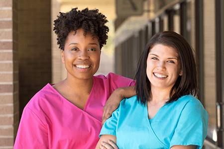 Two smiling women in colorful medical scrubs