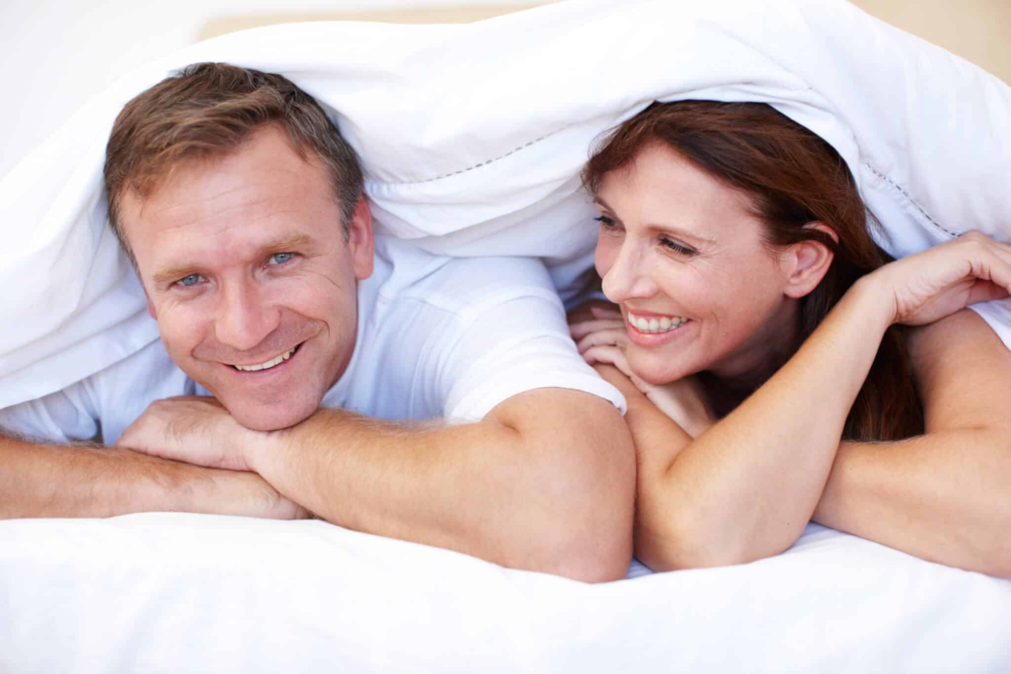 Smiling couple lying under a white bed cover