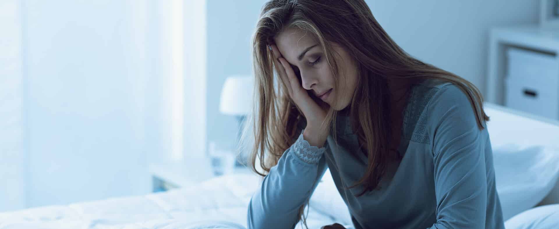 Woman sitting on a bed with her head in her hand, looking distressed