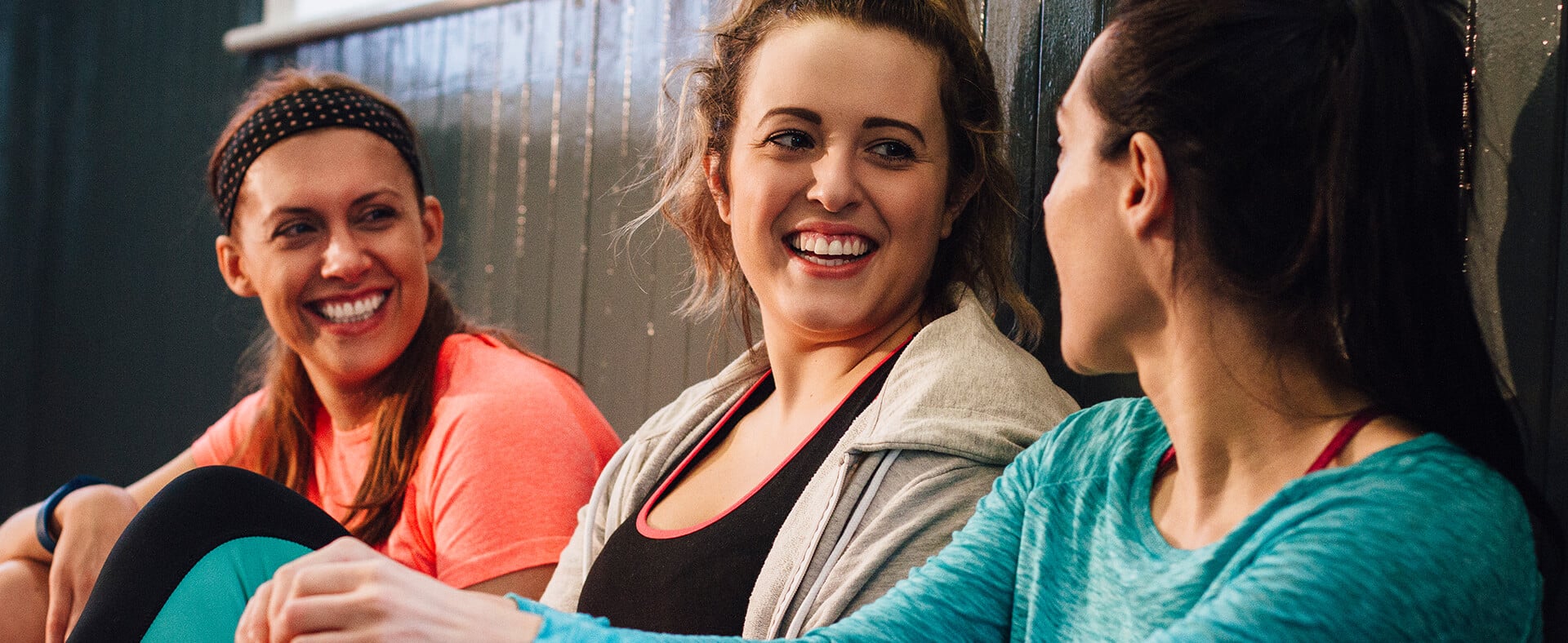 Three smiling women in athletic wear sitting together