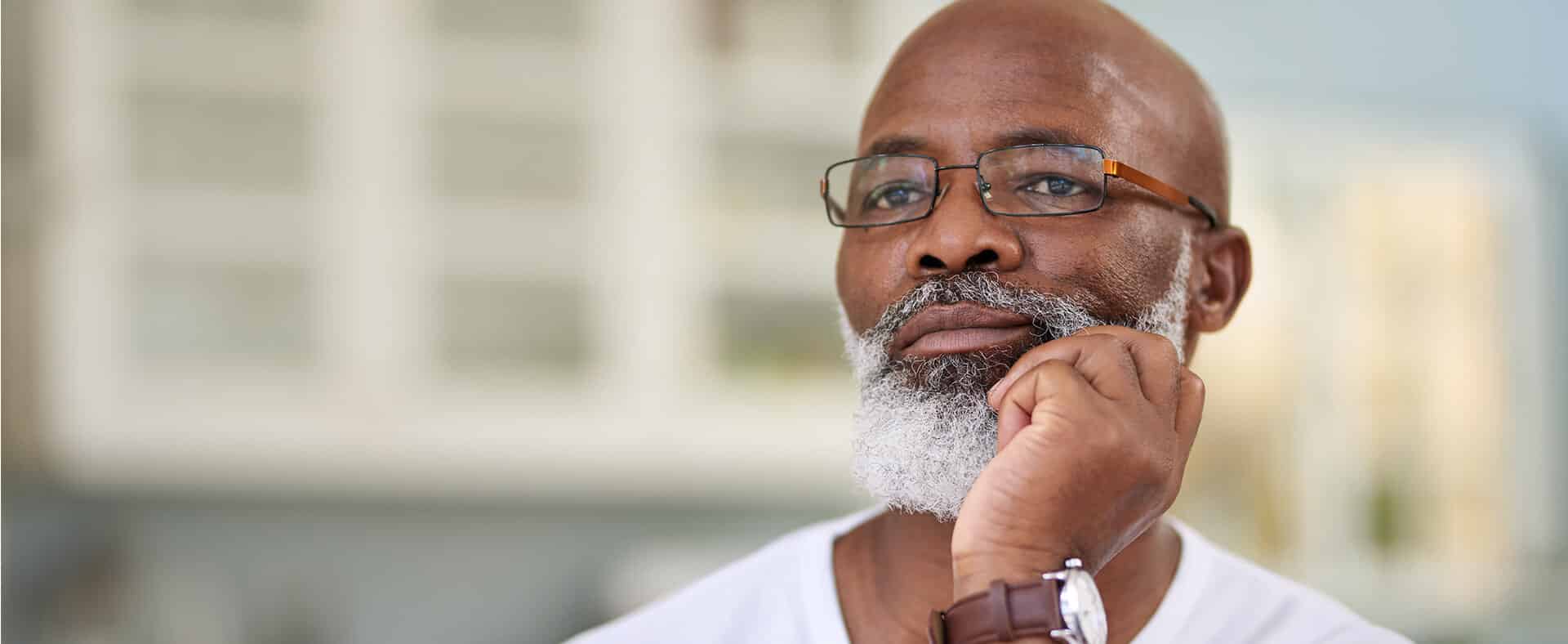 Older man with glasses and a gray beard resting his chin on his hand